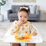 A toddler with a white headband in a high chair enjoys a meal from a Bumkins Silicone Grip Dish: Winnie The Pooh, wearing a yellow bib.