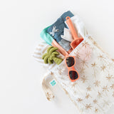 A bag from Bumkins Wet Bag + Wet/Dry Bag Set: Palm Daze is shown with beach gear like sand toys and a swimsuit on a white background.