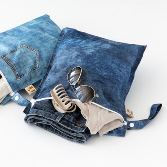 Roamio by Bumkins Wet Bag 2 Pack: Denim On Denim holds sunglasses, a beige hair clip, and clothes on a white background.